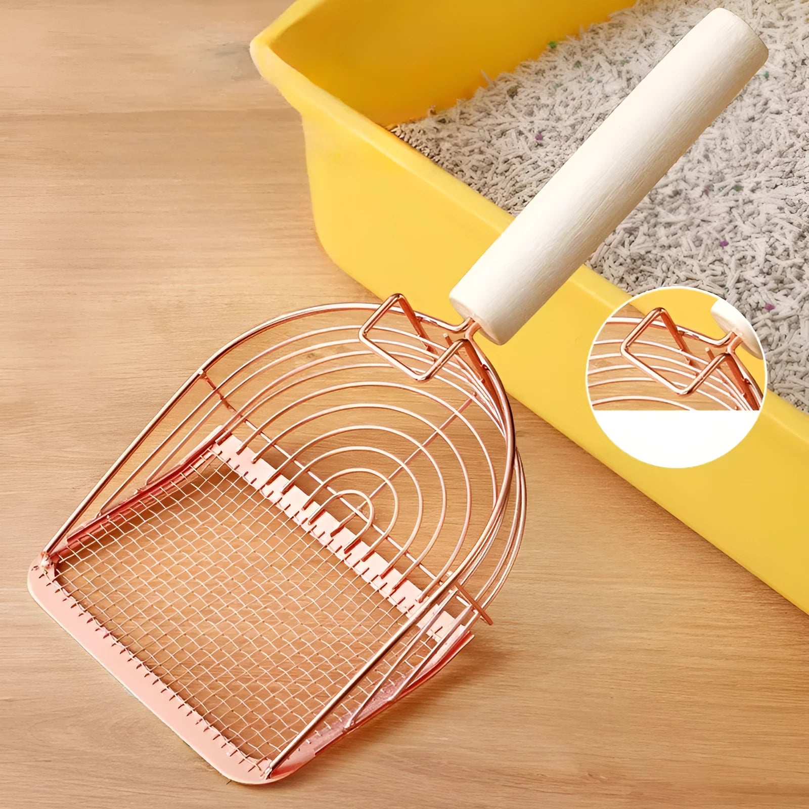 Stainless steel cat litter scoop with a long wooden handle on a litter box.