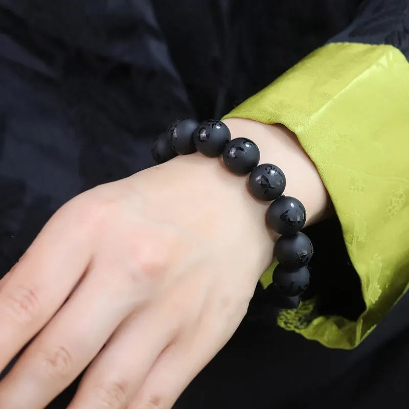 Close-up of a frosted black agate bracelet with an engraved Sanskrit mantra, showing stone texture.