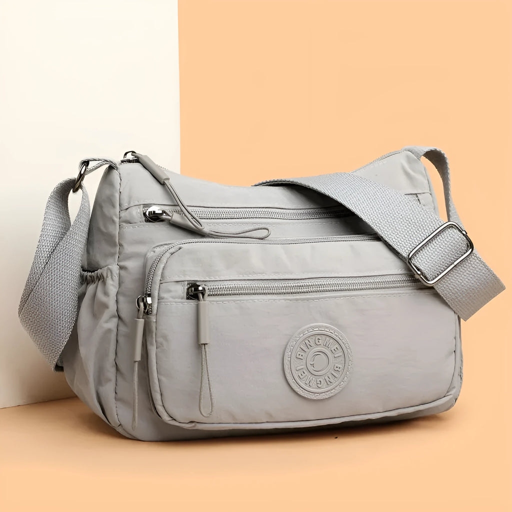 Soft water-repellent nylon crossbody bag in black, grey, or red, showing interior zipper pockets and an exterior 3D pocket.