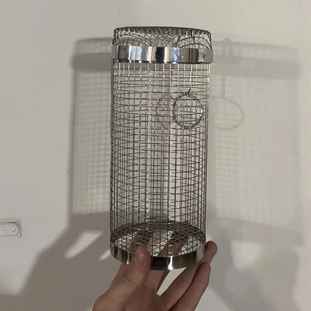 Round rolling metal barbecue grill basket with mesh sides and a handling hook, shown with BBQ gloves.