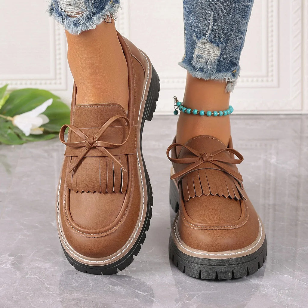 Black plus-size women's loafers with a bow and tassel decoration on the round toe.