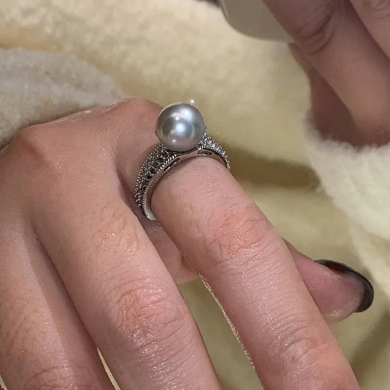 Silver-tone adjustable open ring with a geometric shape and a single black pearl on a model's finger.