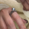Silver-tone adjustable open ring with a geometric shape and a single black pearl on a model's finger.