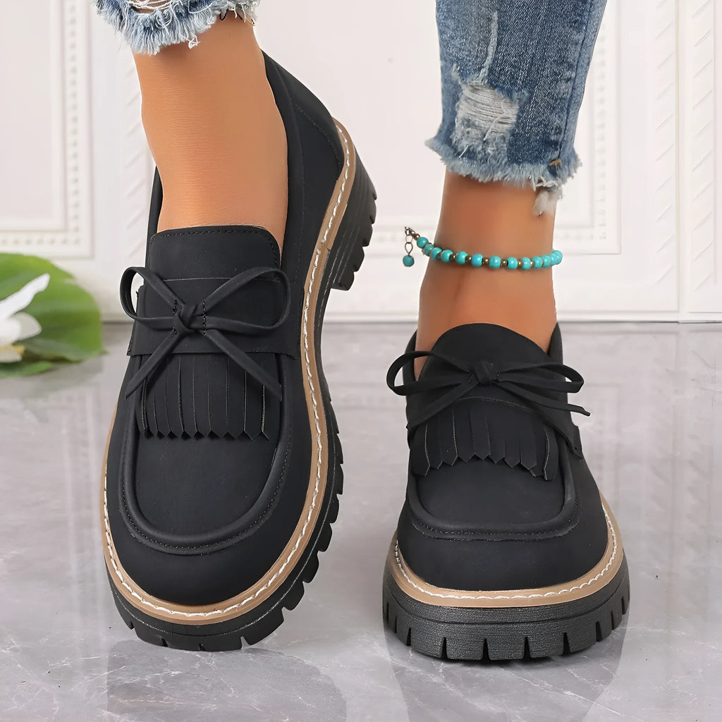 Black plus-size women's loafers with a bow and tassel decoration on the round toe.