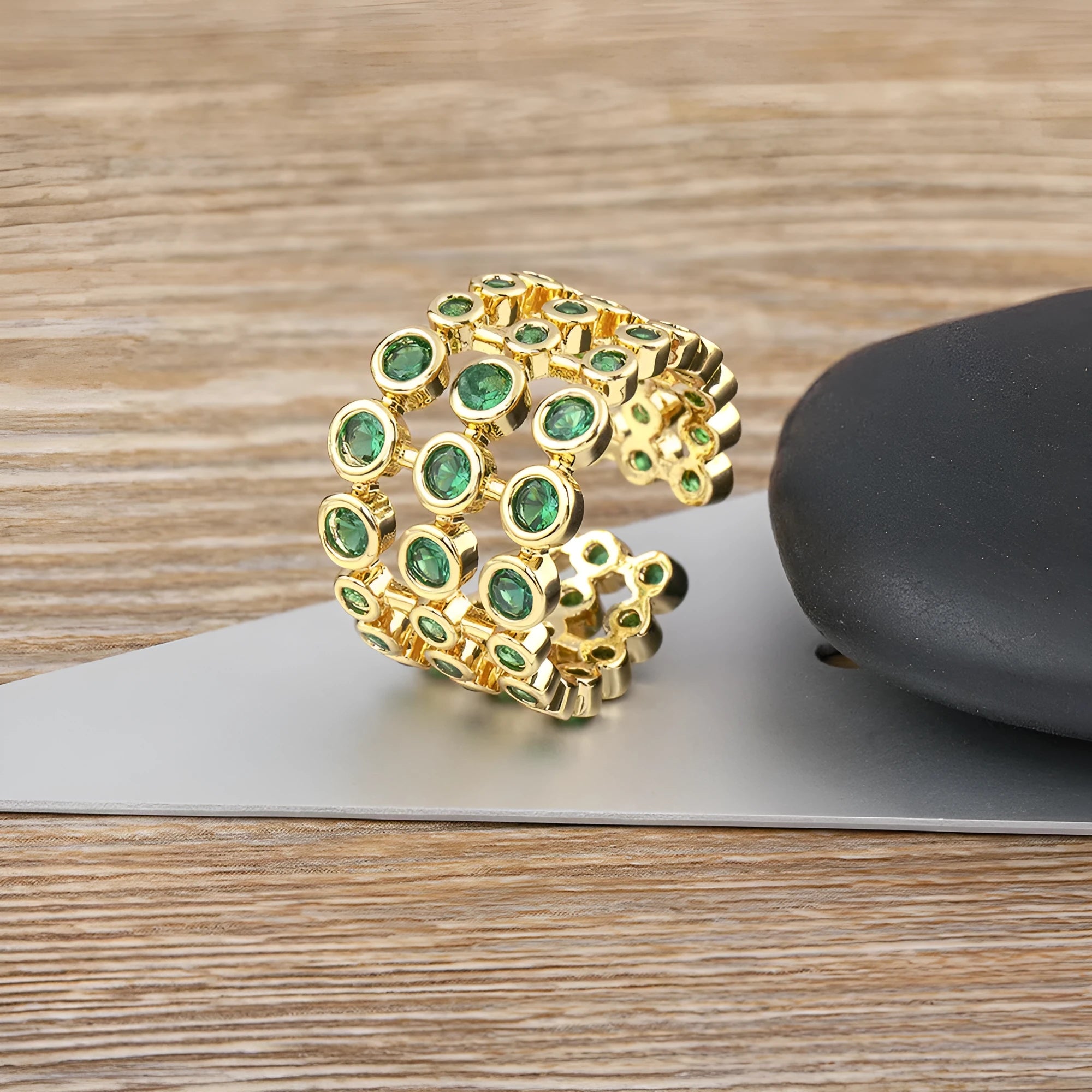 Gold-coloured wide-band ring with green accents and zircon stones on a copper base.