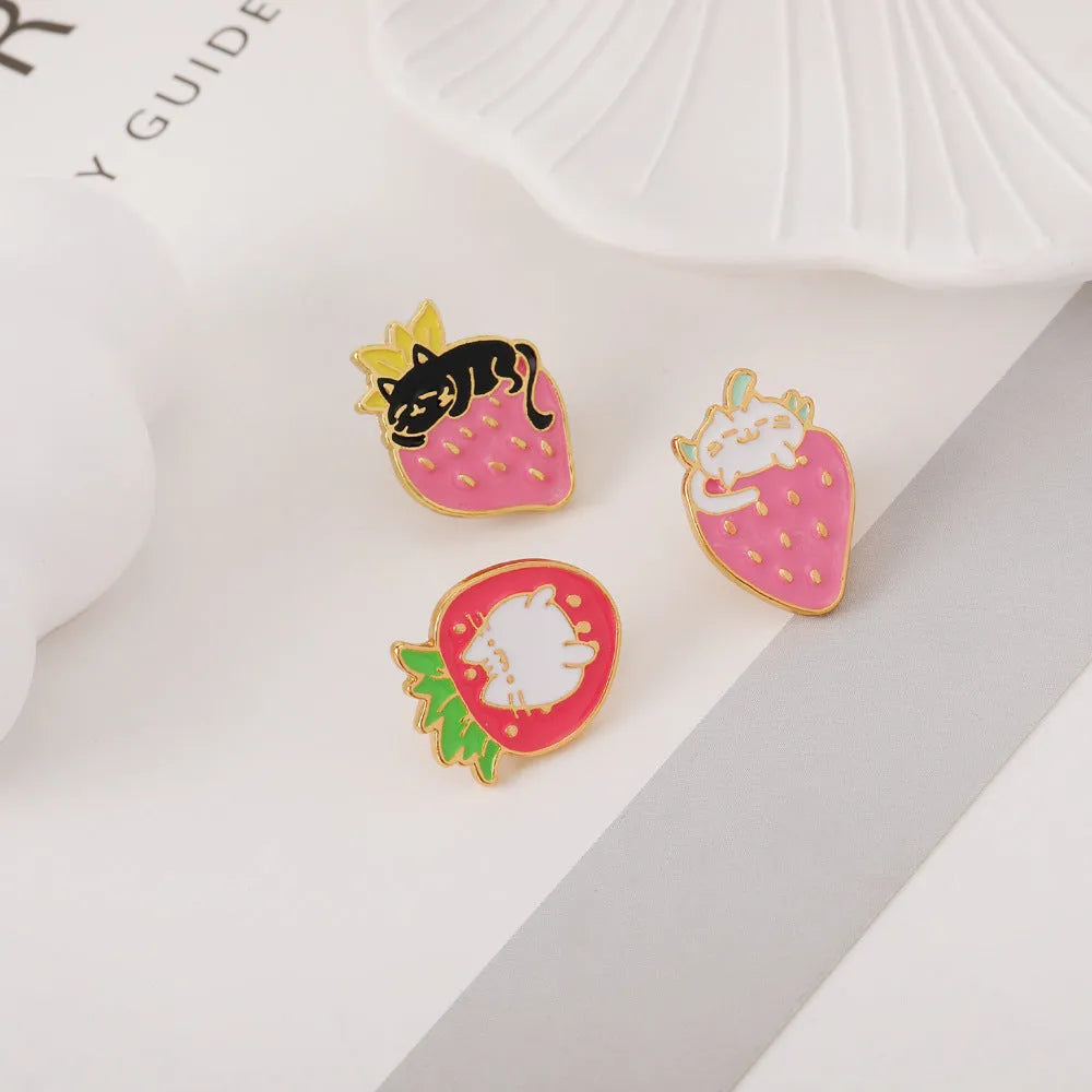 Close-up of a detailed alloy brooch showing a cute cat and strawberry in a dripping oil art style.
