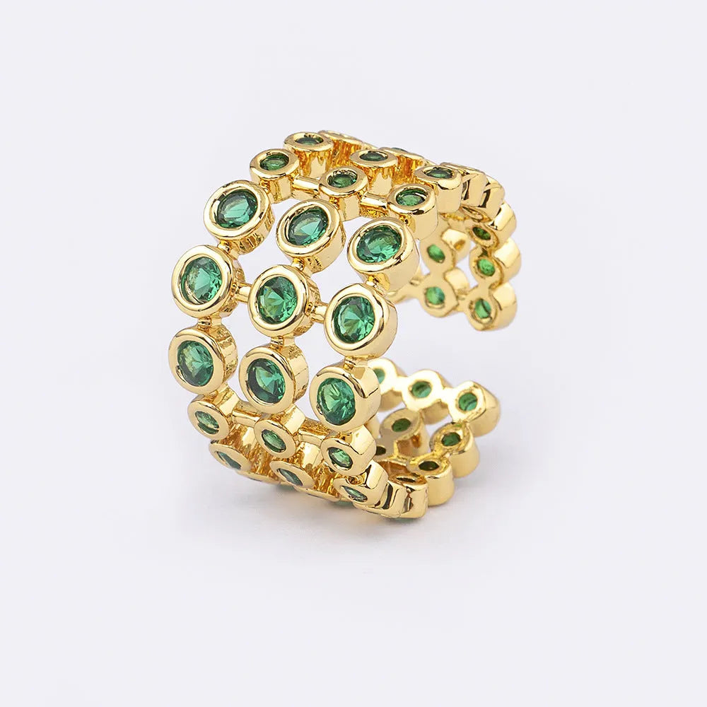 Gold-coloured wide-band ring with green accents and zircon stones on a copper base.
