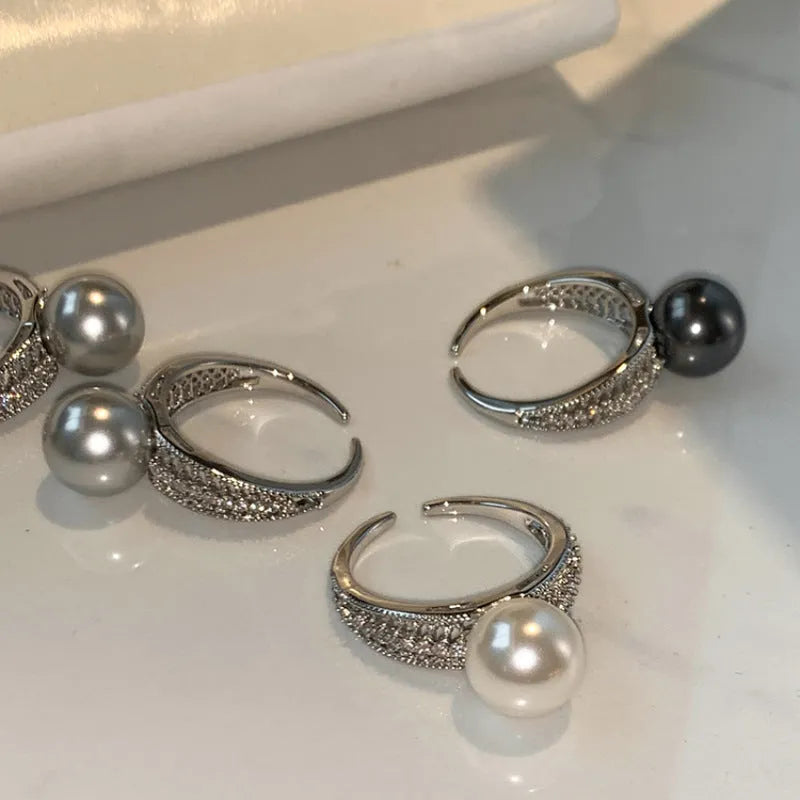 Silver-tone adjustable open ring with a geometric shape and a single black pearl on a model's finger.