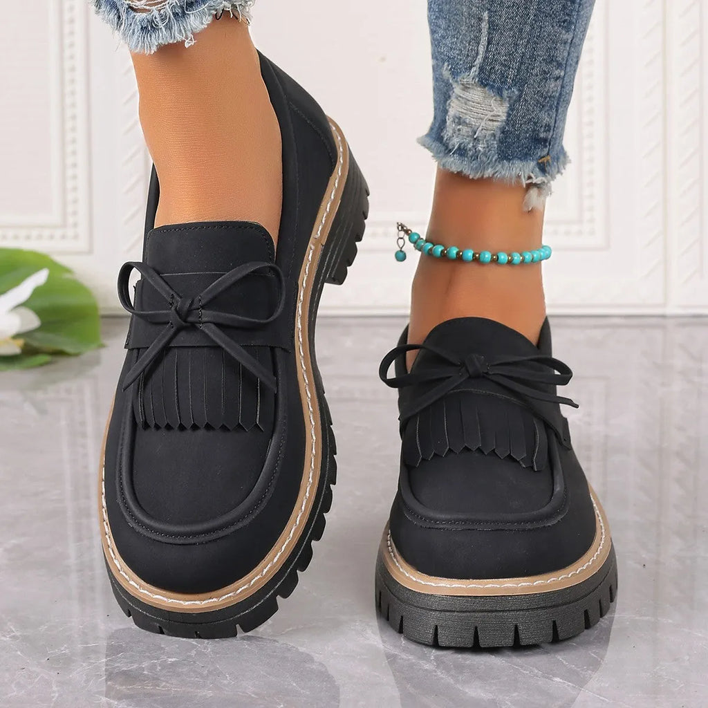 Black plus-size women's loafers with a bow and tassel decoration on the round toe.