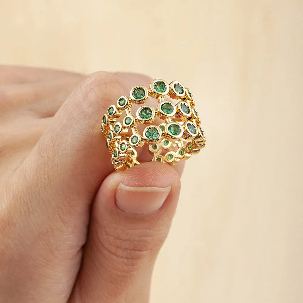 Gold-coloured wide-band ring with green accents and zircon stones on a copper base.