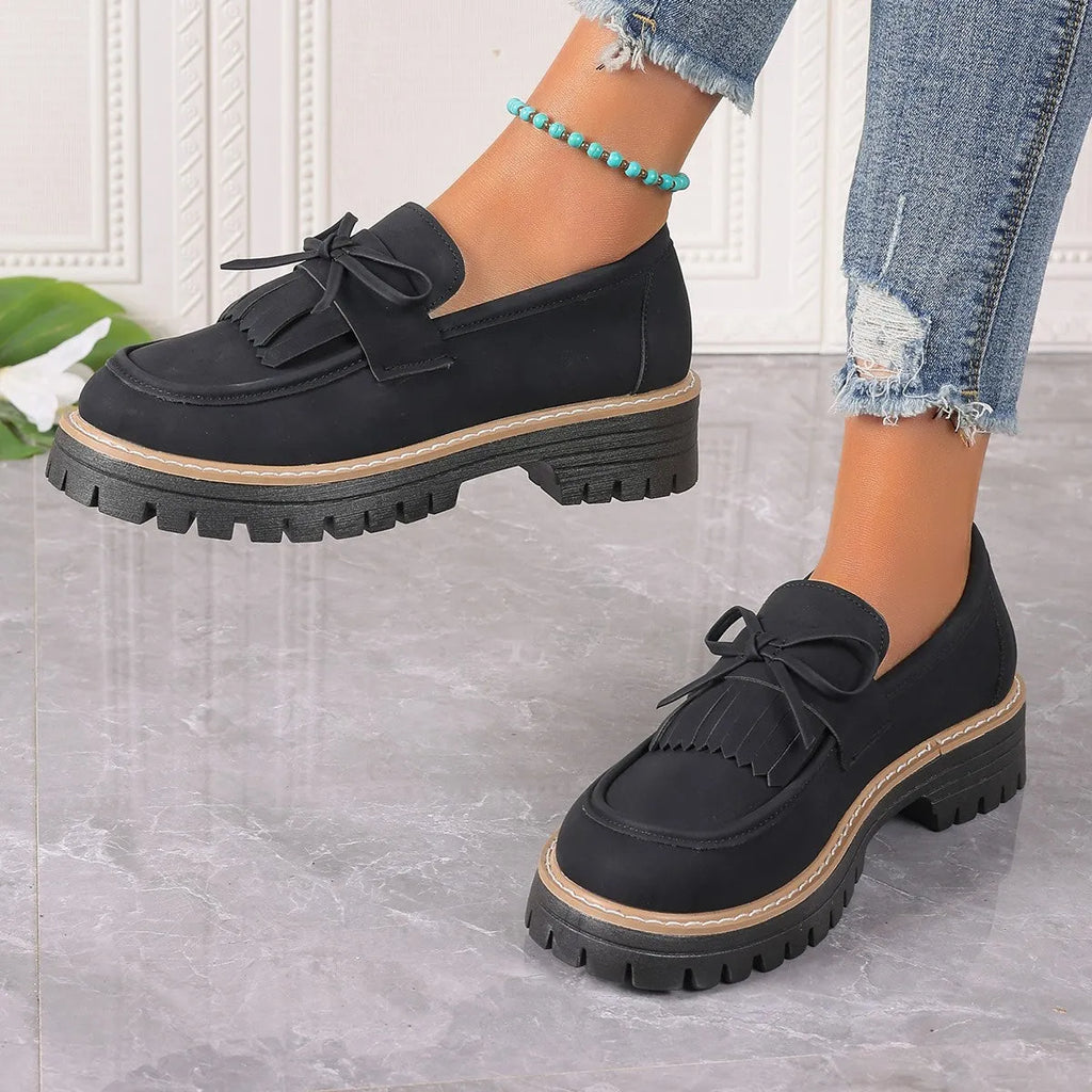 Black plus-size women's loafers with a bow and tassel decoration on the round toe.
