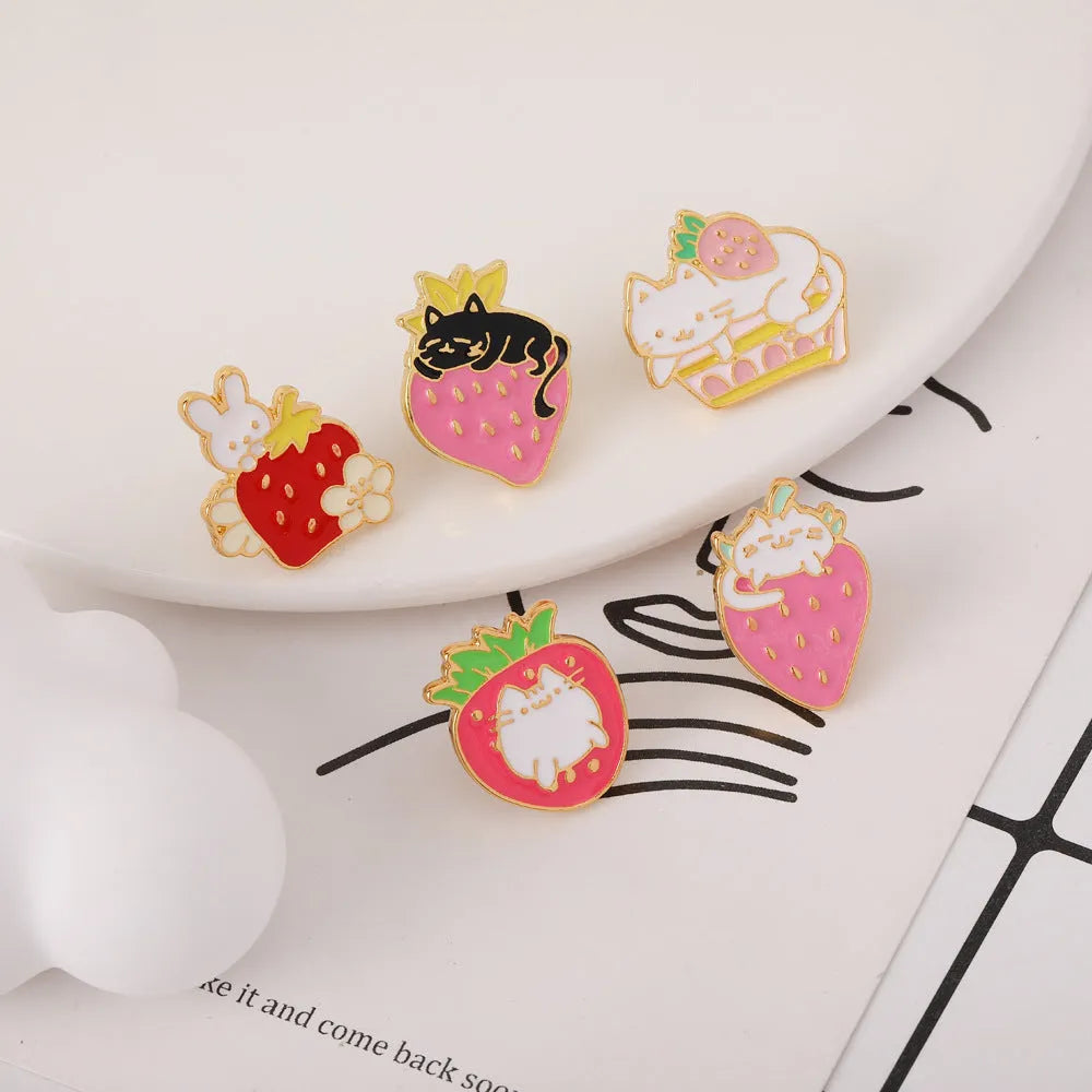 Close-up of a detailed alloy brooch showing a cute cat and strawberry in a dripping oil art style.