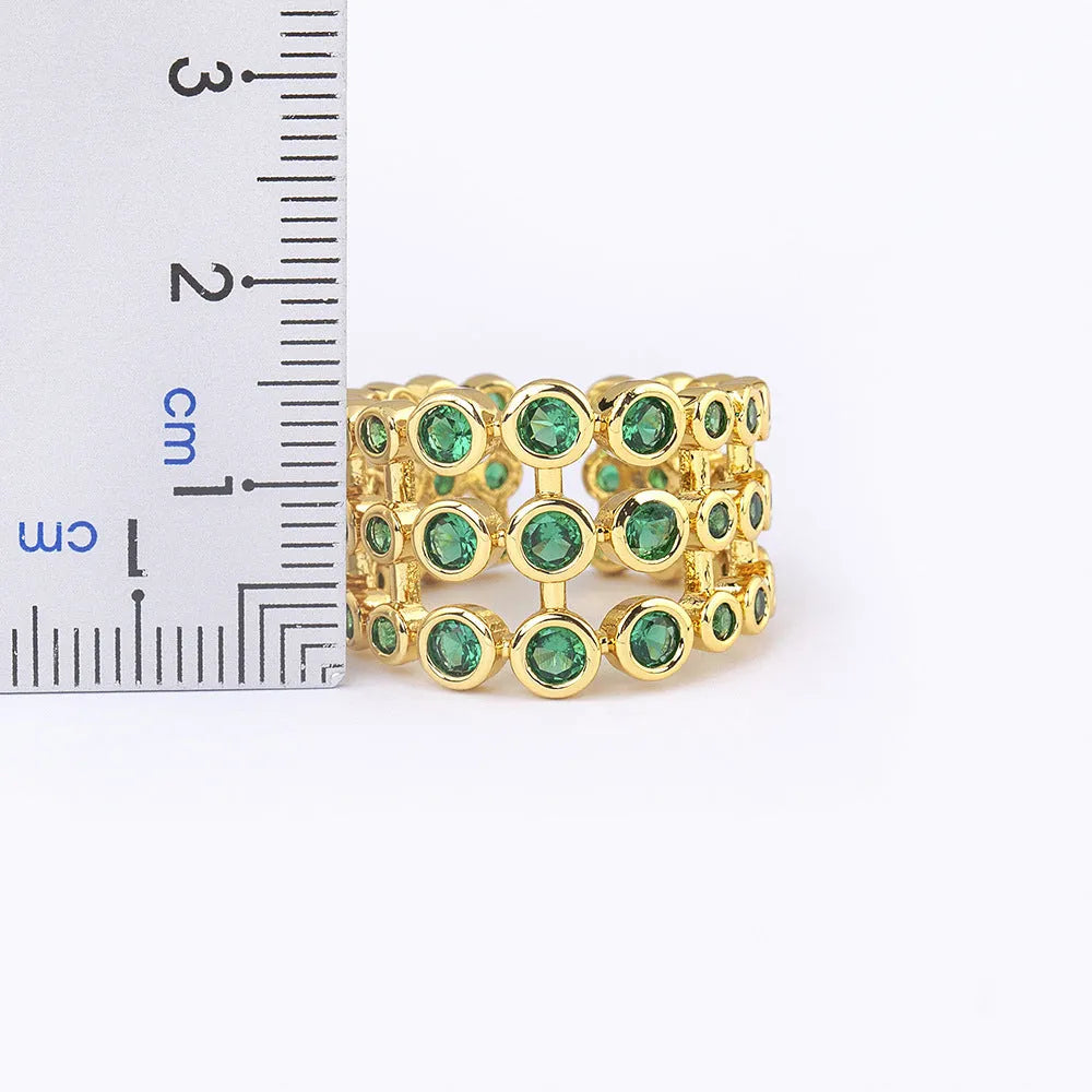 Gold-coloured wide-band ring with green accents and zircon stones on a copper base.