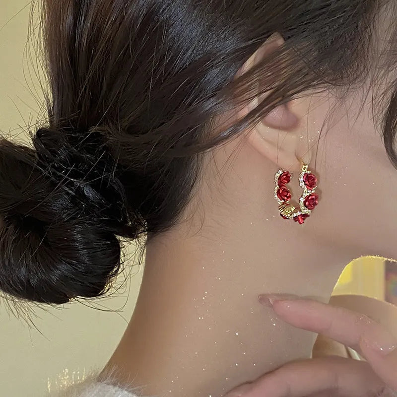 A pair of red flower-shaped alloy clip-on earrings with rose detailing for women.