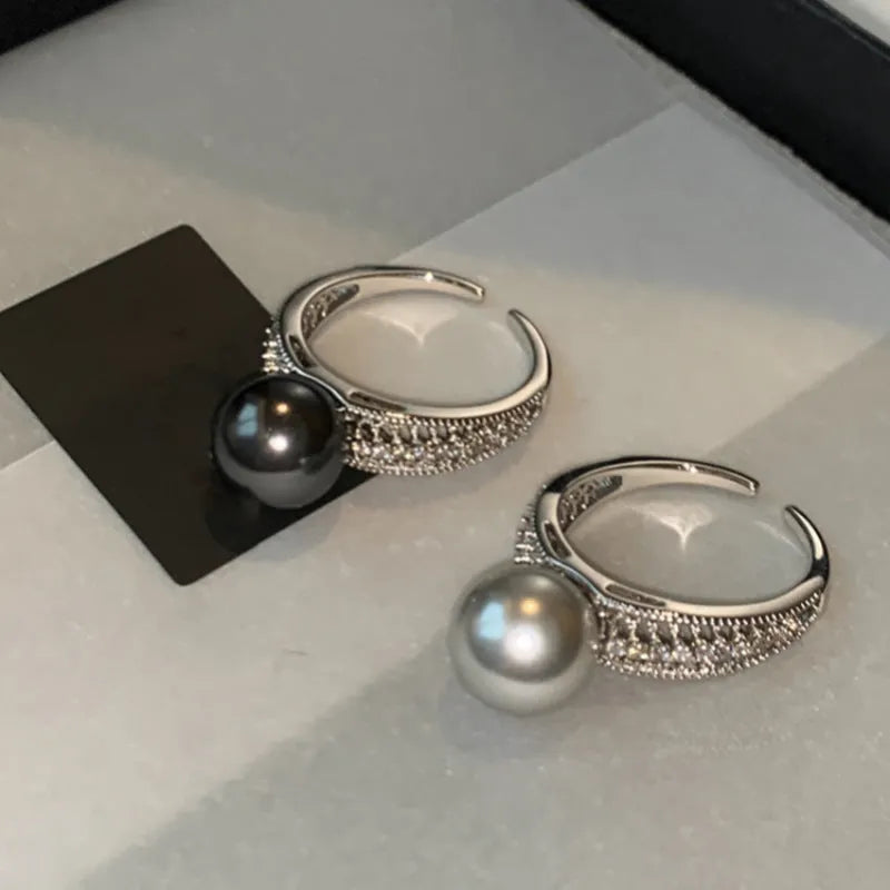 Silver-tone adjustable open ring with a geometric shape and a single black pearl on a model's finger.