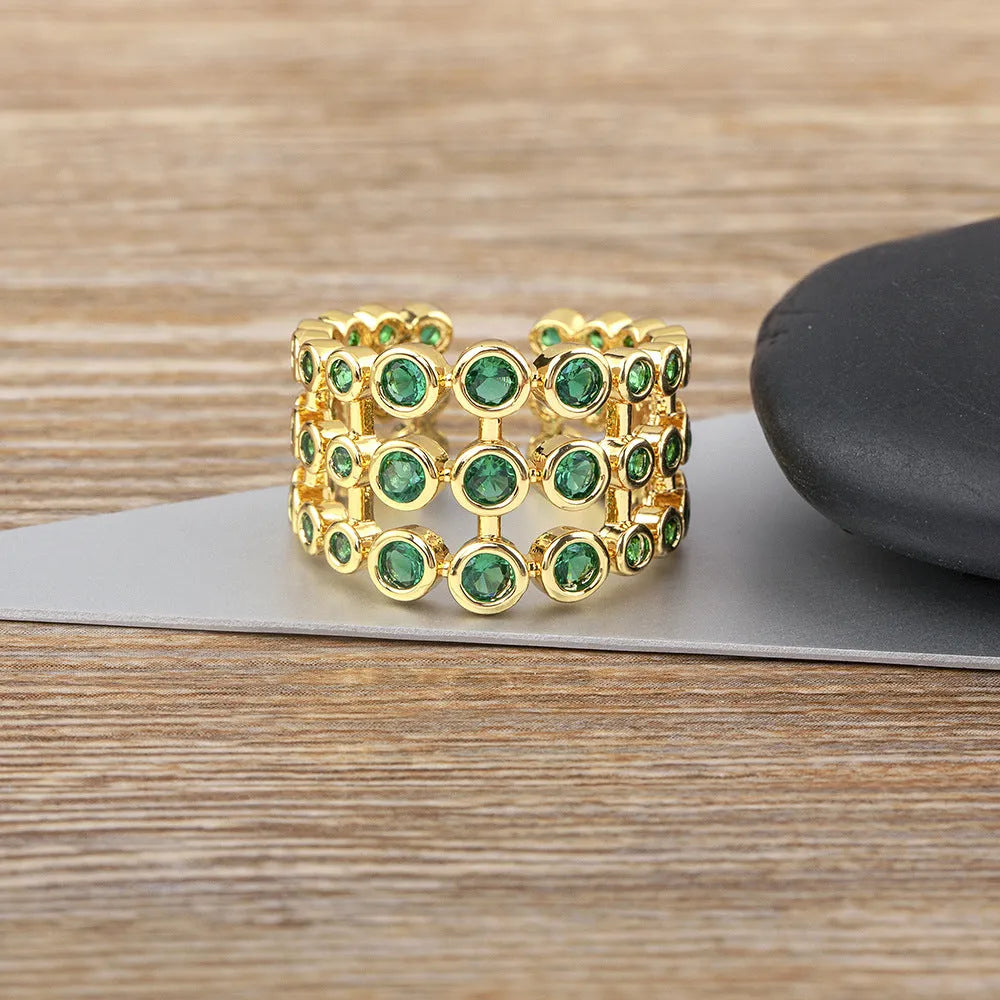 Gold-coloured wide-band ring with green accents and zircon stones on a copper base.