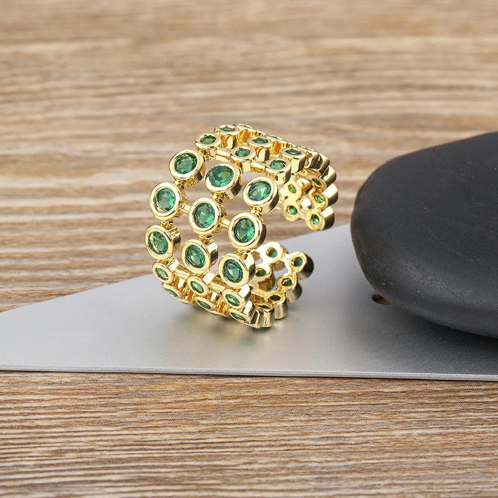 Gold-coloured wide-band ring with green accents and zircon stones on a copper base.