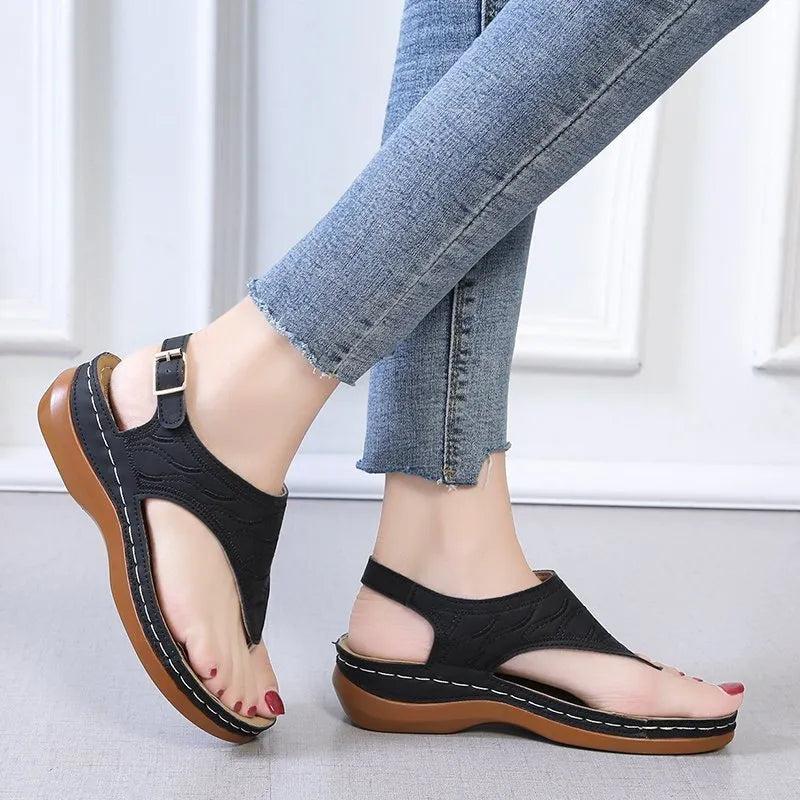 Women's beige wedge heel flip flop sandals with an adjustable buckle strap on a wooden deck.