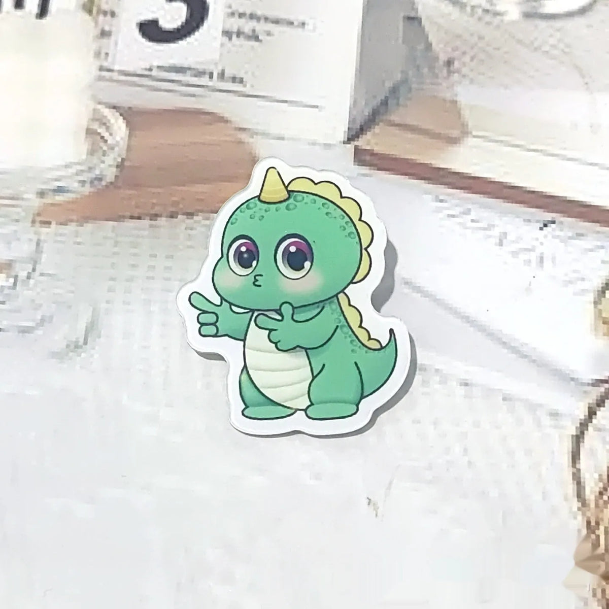 Cartoon dinosaur acrylic badge brooch with printed design and pin fastening, shown in one of twelve colour styles