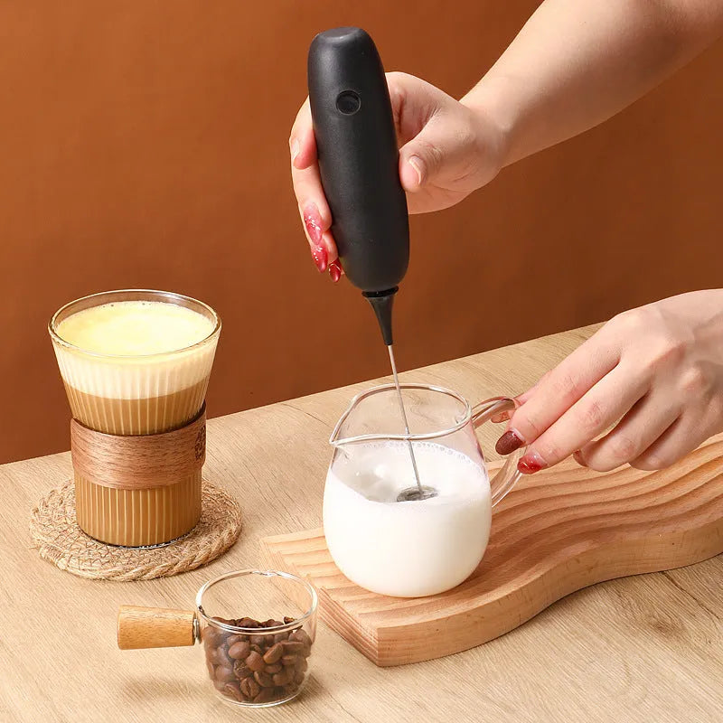 Hand-held electric milk frother and blender in black and white colour options on a kitchen counter.