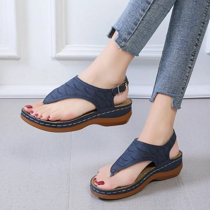 Women's beige wedge heel flip flop sandals with an adjustable buckle strap on a wooden deck.