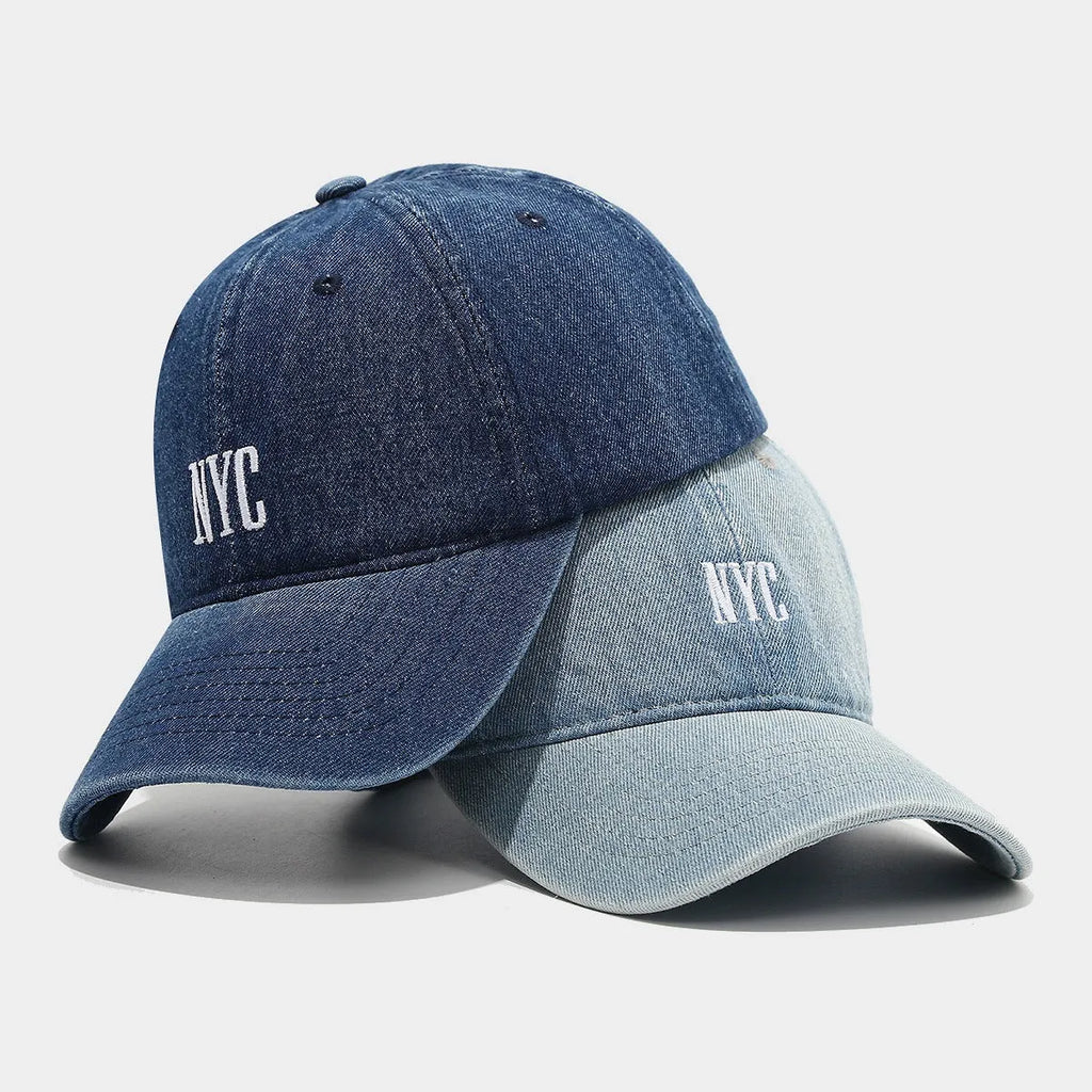 Light blue denim peaked cap with embroidered letters on a dome crown, showing adjustable strap.
