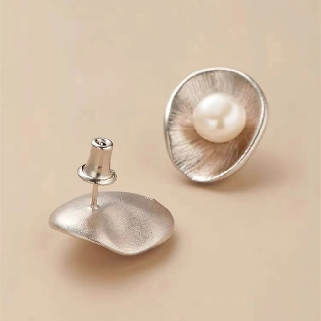 Gold tone geometric stud earrings with a central freshwater pearl on a silver needle post.