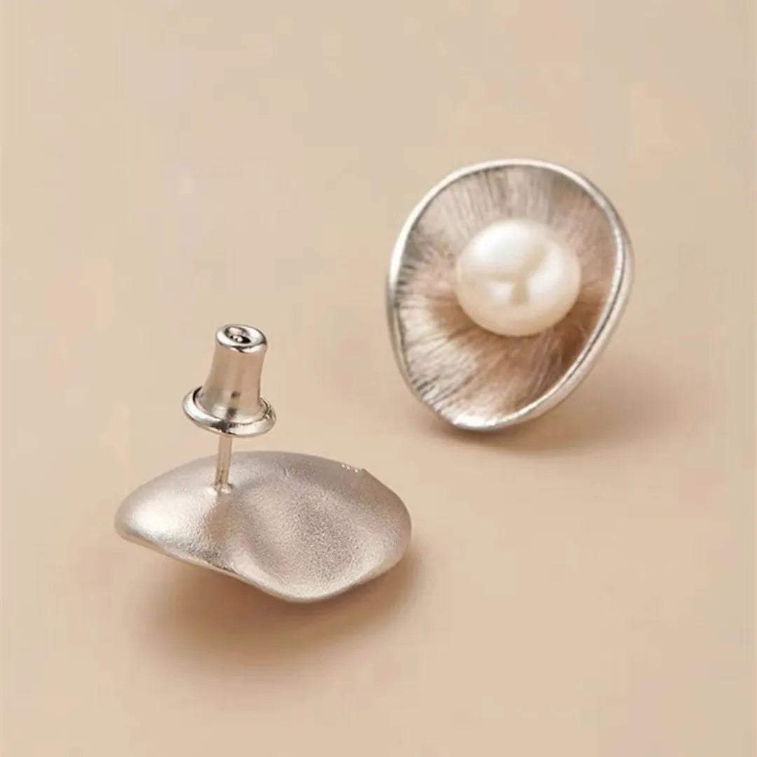 Gold tone geometric stud earrings with a central freshwater pearl on a silver needle post.