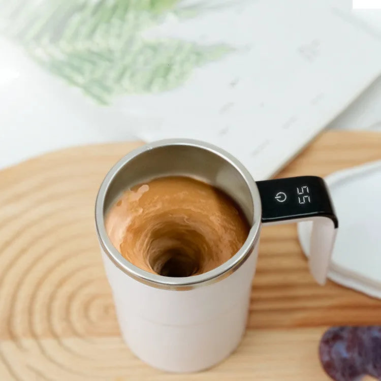 Black and white USB rechargeable electric stirring mug with LCD screen showing temperature, next to its magnetic stirrer.