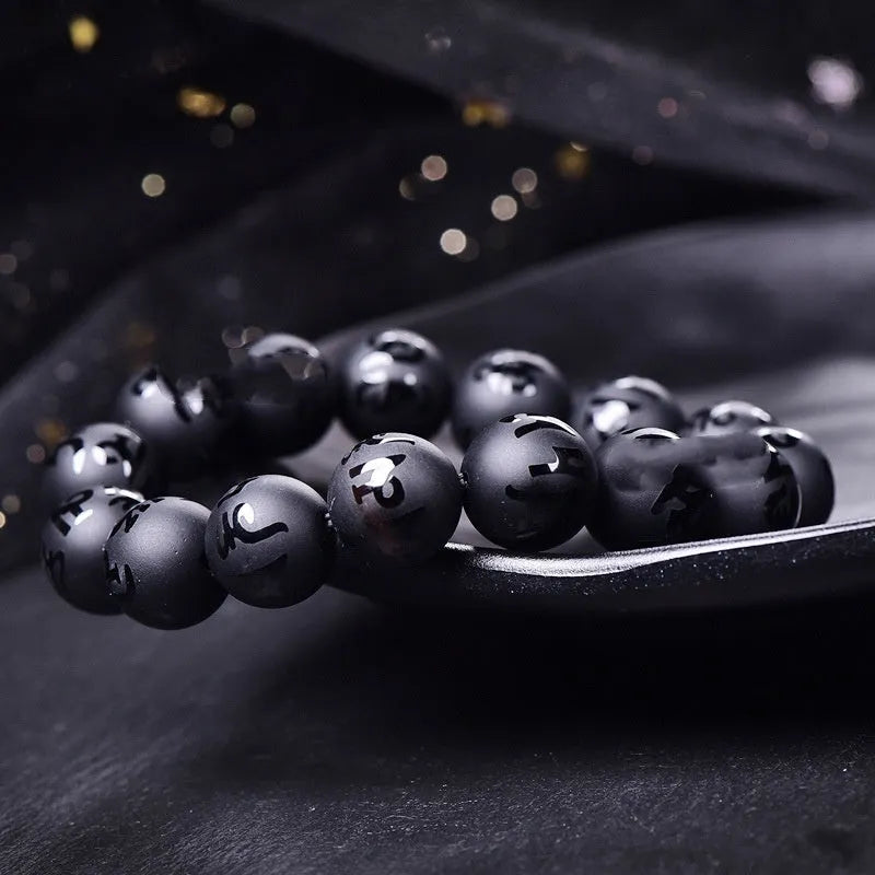 Close-up of a frosted black agate bracelet with an engraved Sanskrit mantra, showing stone texture.