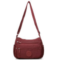 Soft water-repellent nylon crossbody bag in black, grey, or red, showing interior zipper pockets and an exterior 3D pocket.