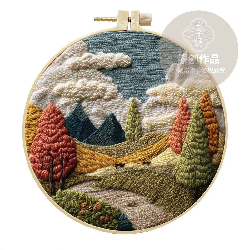 DIY embroidery kit components: printed cotton landscape fabric, embroidery threads, needles, and a bamboo hoop.