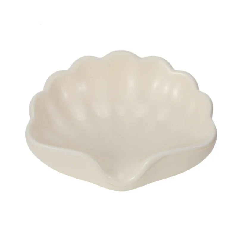 White shell-shaped plastic soap dish with drainage holes on a bathroom surface