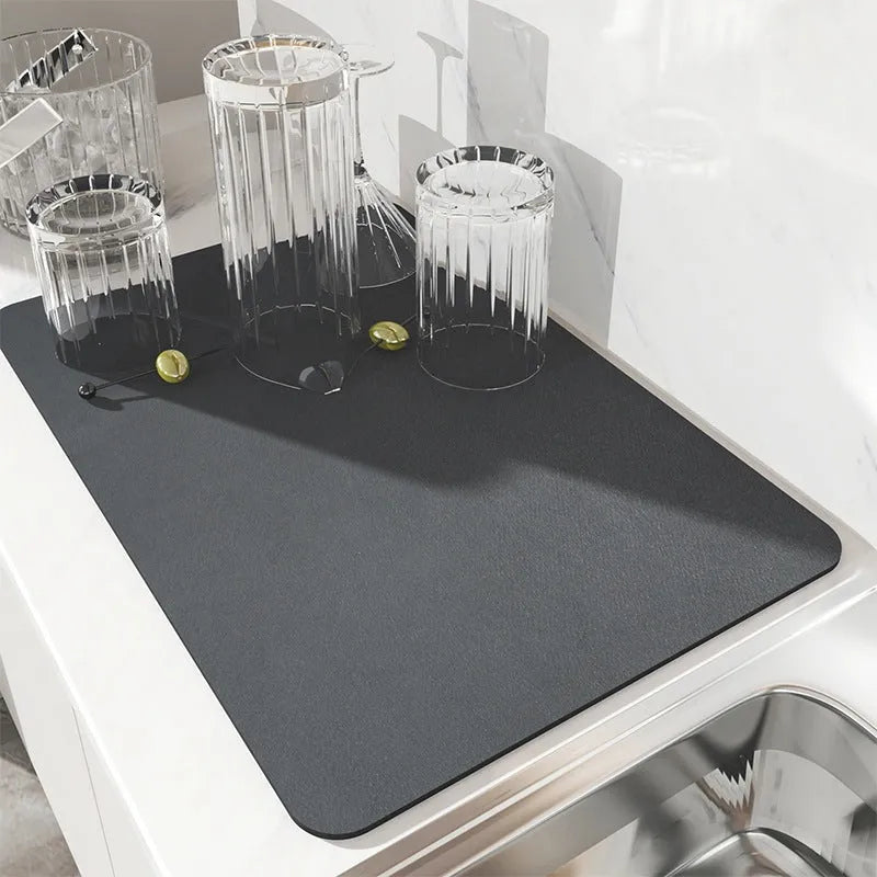 Black square rubber-backed kitchen drying mat on a countertop next to a coffee cup