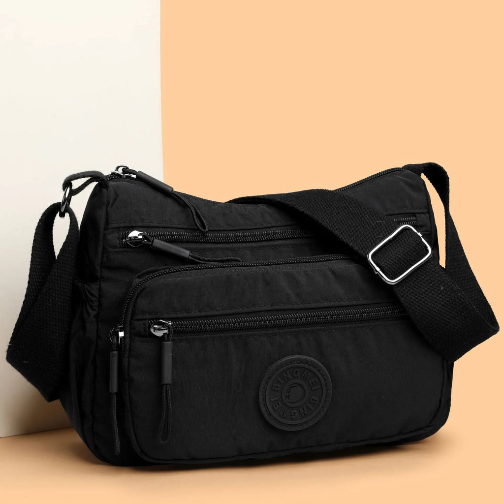 Soft water-repellent nylon crossbody bag in black, grey, or red, showing interior zipper pockets and an exterior 3D pocket.