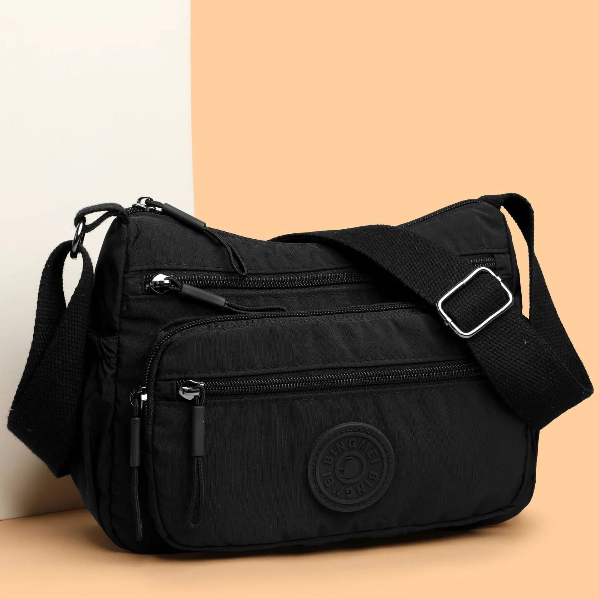 Soft water-repellent nylon crossbody bag in black, grey, or red, showing interior zipper pockets and an exterior 3D pocket.