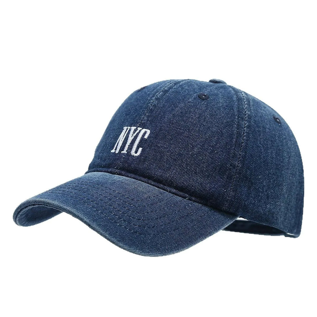 Light blue denim peaked cap with embroidered letters on a dome crown, showing adjustable strap.