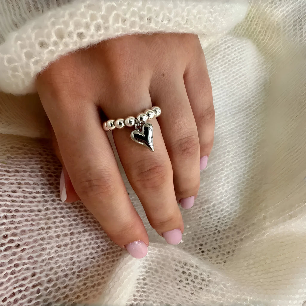 Handmade elastic love ring with geometric beaded string design and heart charm on adjustable band