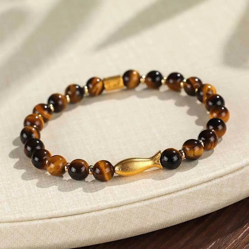 Close-up of a yellow tiger eye beaded bracelet with a detailed small fish charm.