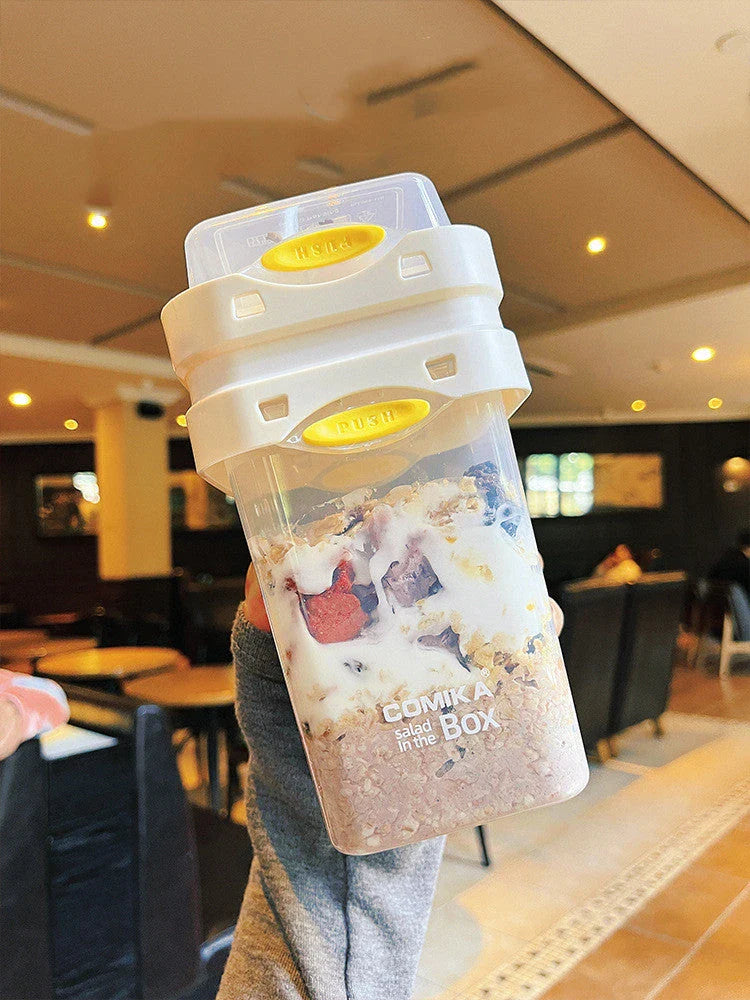 A portable bento box with two compartments for storing different types of food, such as salad, yogurt, oatmeal, and milkshake.