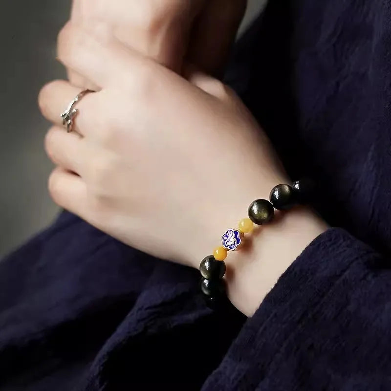 Handmade golden obsidian bracelet with geometric beads and zodiac charm on wrist.