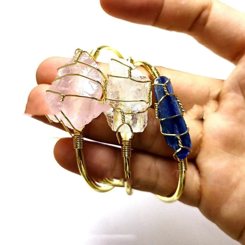 Rough natural crystal bracelet with gold winding geometric design on a wrist.