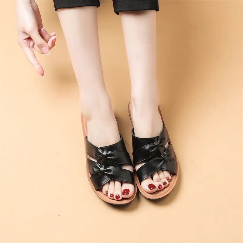 Beige cowhide leather women's slippers with a non-slip sole on a wooden floor.