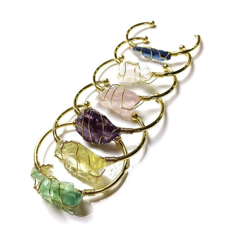 Rough natural crystal bracelet with gold winding geometric design on a wrist.