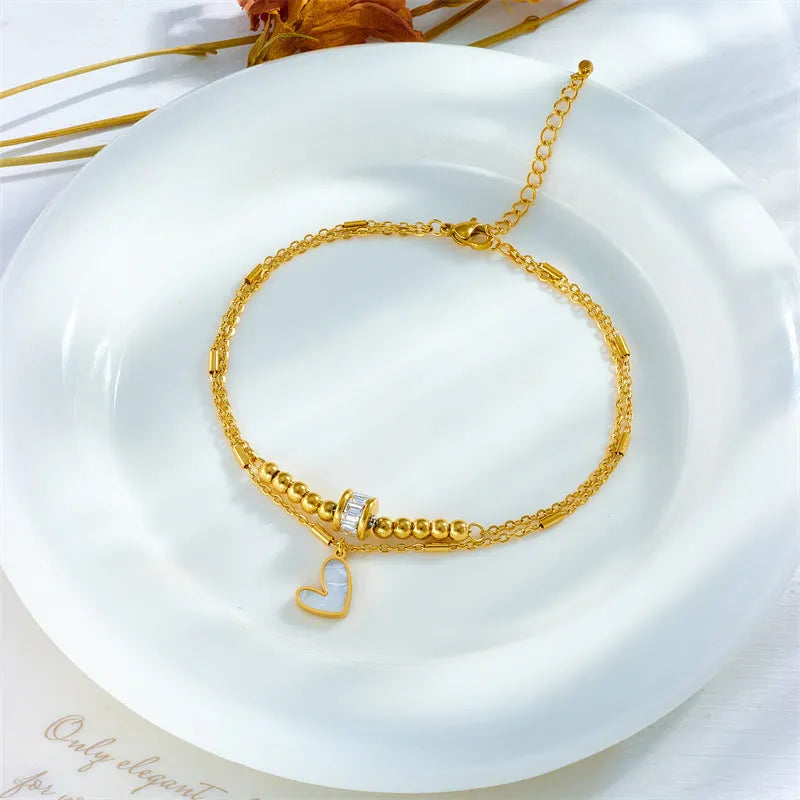 Gold titanium steel double-layer ankle chain with love heart charm and tassel on a white background
