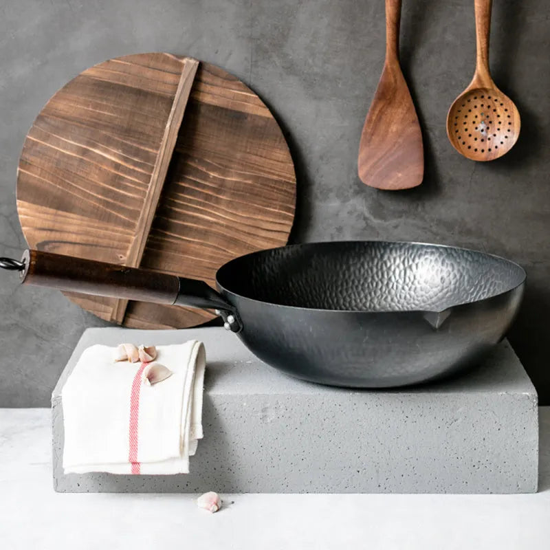 Handmade traditional black iron wok with a long wooden handle on a kitchen counter.
