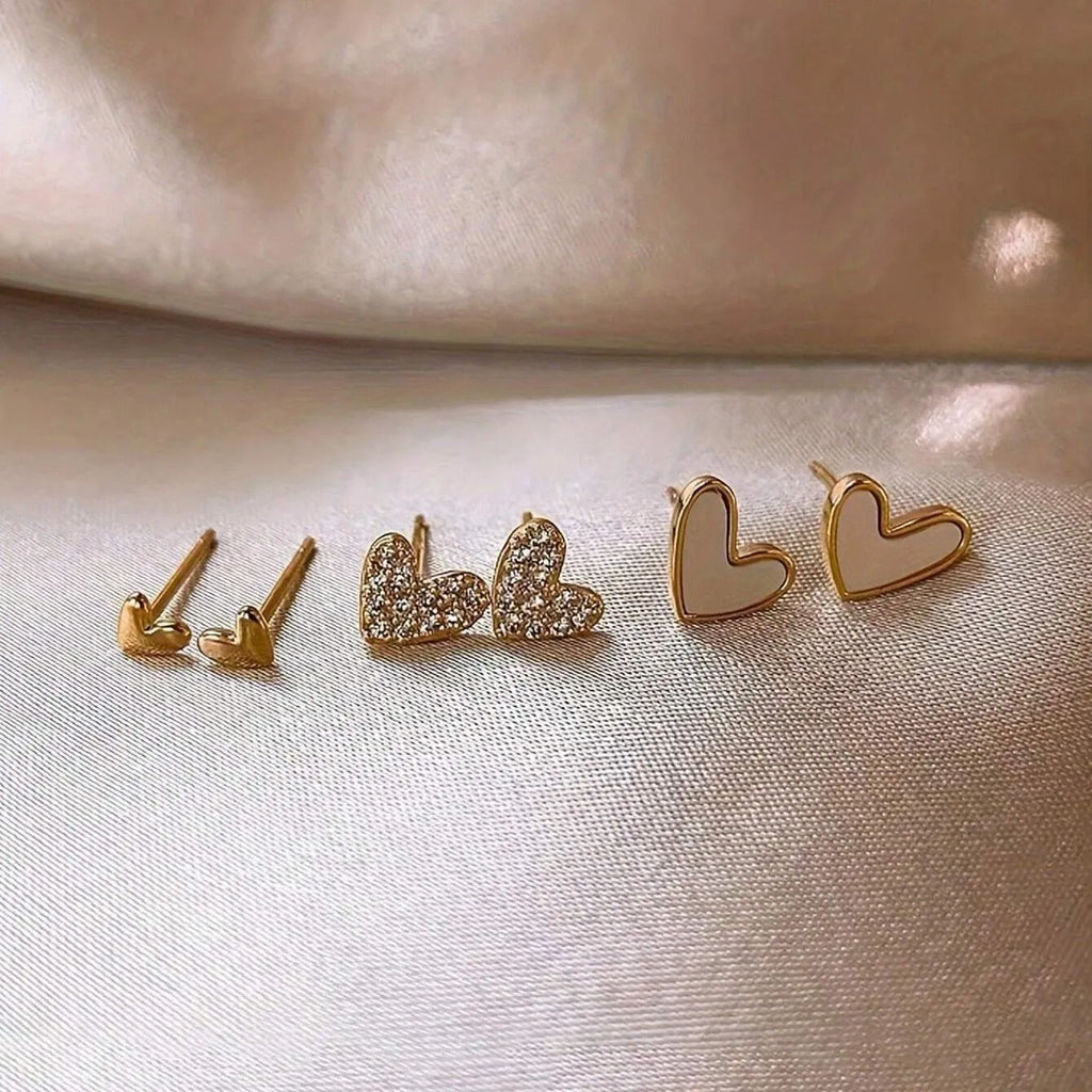 Set of three pairs of women's heart-shaped alloy earrings in gold, black, black and white, and pink colours.