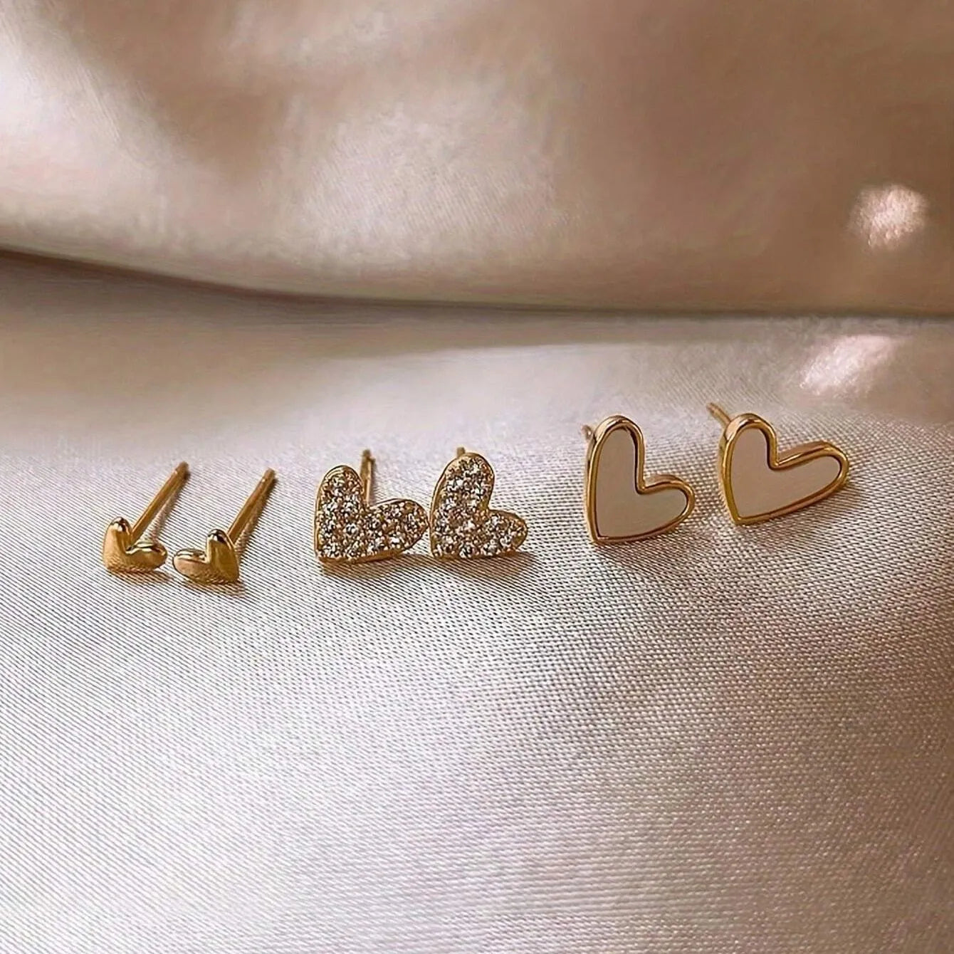 Set of three pairs of women's heart-shaped alloy earrings in gold, black, black and white, and pink colours.