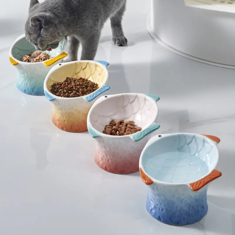 Set of four blue fish-shaped ceramic cat bowls on a table, showing elevated shallow design and tilt angle.