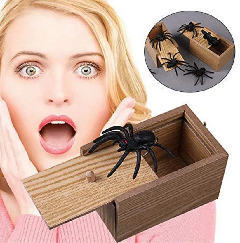 Wooden prank box with lid open showing a lifelike jumping spider inside on a white background.